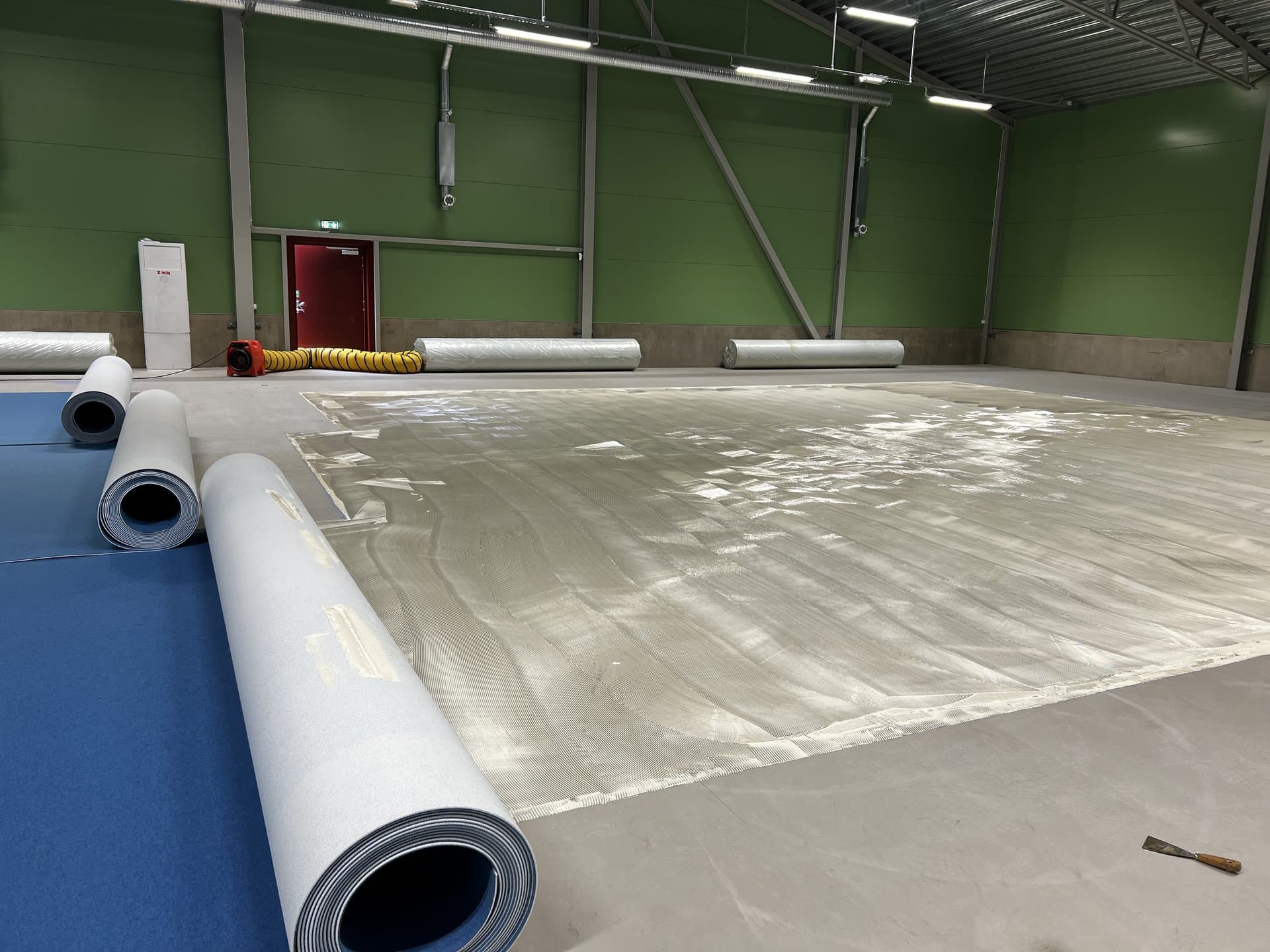 Sportgolv under installation, en del av blå matta är utlagd över limmad betongyta