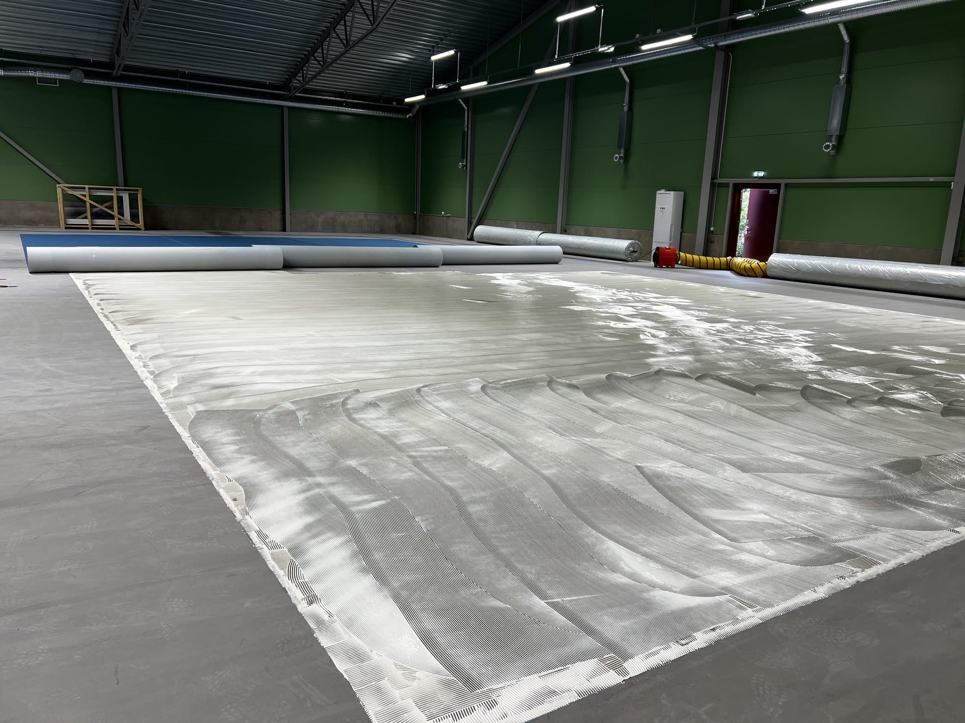 Stor sportgolv-hall med klar limyta över betongen, klar för matta-installation